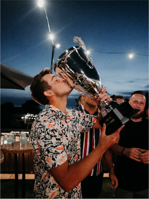 A man holding up a large trophy, kissing it as the sun sets in the distance