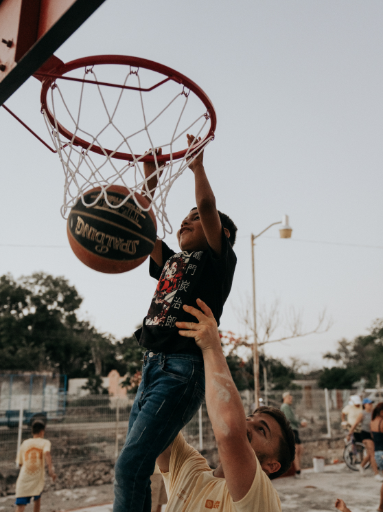 A young boy being lifted up to dunk a basket ball