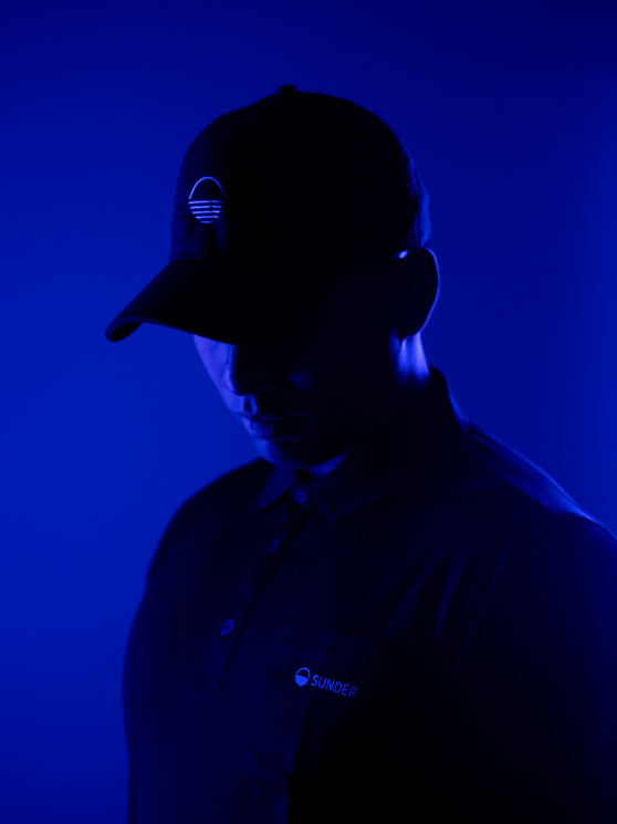 A rep in a dark polo shirt and cap posing against a blue background