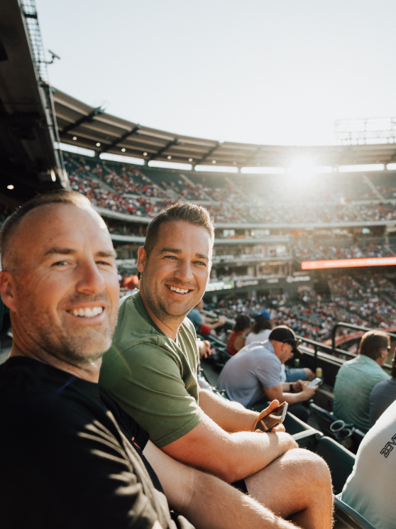 Two men sitting in a crowded stadium on a sunny day